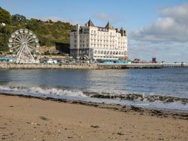 A sandy beach with waves and a pier with a ferris wheel and a large hotel building by the sea at Seawinds in Rhos-On-Sea