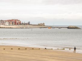 A sandy beach with a person and dog near the water and boats on the sea with buildings in the background at Seawinds in Rhos-On-Sea