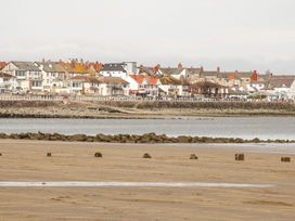 A sandy beach with stone barriers and water in front of a row of houses at Seawinds in Rhos-On-Sea