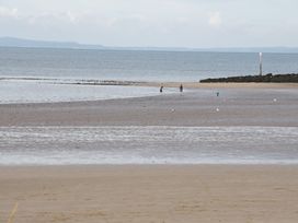 A beach with wet sand and three people walking near the water at Seawinds in Rhos-On-Sea