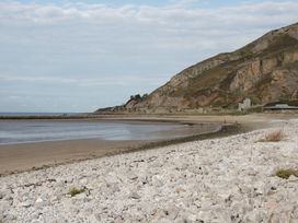 A rocky beach with a sandy shore and cliffs in the background at Seawinds in Rhos-On-Sea