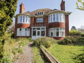 A two-story brick house with bay windows and a gravel pathway leading to the entrance surrounded by grass and bushes at Seawinds in Rhos-On-Sea