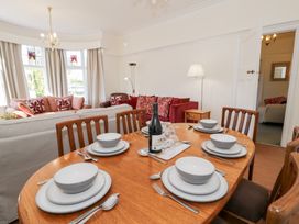 A dining table set with plates bowls cutlery and a wine bottle in a living room with sofas and cushions at Seawinds in Rhos-On-Sea