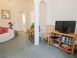 A living room with a sofa and red pillows a TV on a wooden stand with books and a decorative plate a round wooden table with a plant and two wooden chairs at Seawinds in Rhos-On-Sea