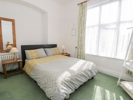 A bedroom with a double bed with patterned bedding two wooden bedside tables with lamps a full length mirror and a large window with curtains at Seawinds in Rhos-On-Sea