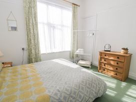 A bedroom with a bed a wooden chest of drawers a clothes rack with towels and a window with curtains at Seawinds in Rhos-On-Sea