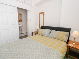 A bedroom with a bed covered with a patterned duvet two wooden bedside tables with lamps a mirror on the wall and a door leading to a bathroom at Seawinds in Rhos-On-Sea