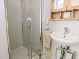 A bathroom with a corner shower enclosure a wall-mounted sink a wooden mirror cabinet and a towel hanging on a ring at Seawinds in Rhos-On-Sea