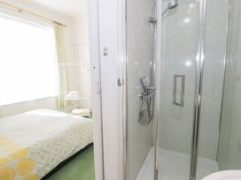 A bedroom with a bed and curtains visible through an open door next to a shower with glass doors at Seawinds in Rhos On Sea