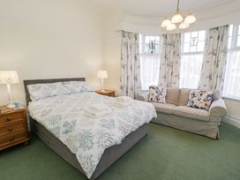 A bedroom with a double bed two bedside tables lamps a sofa and floral curtains at Seawinds in Rhos-On-Sea