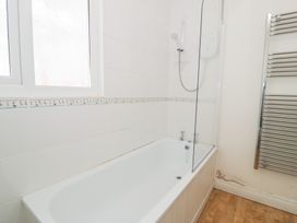 A bathroom with a bathtub shower unit window and heated towel rail with wood effect flooring at Seawinds in Rhos-On-Sea