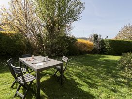 A garden with wooden table and chairs on grass surrounded by trees and bushes at Seawinds in Rhos-On-Sea