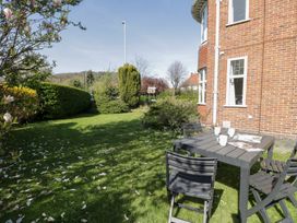 A garden area with a black table and chairs set on grass next to a red brick house at Seawinds in Rhos-On-Sea