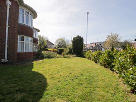 A garden with green grass and bushes next to a red brick house with large windows at Seawinds in Rhos-On-Sea