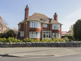 A two-story red brick house with multiple chimneys and large bay windows surrounded by a stone wall and shrubbery at Seawinds in Rhos-On-Sea