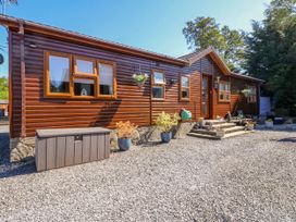 The exterior of a wooden cabin with several windows a door steps with potted plants gravel ground and outdoor seating at RoseGrace Lodge in Auchterarder
