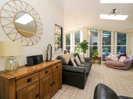 A living room with a wooden sideboard black leather sofa round pink chair and large windows at RoseGrace Lodge in Auchterarder