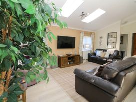 A living room with two leather sofas a wall-mounted television and a large indoor plant at RoseGrace Lodge in Auchterarder