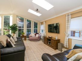 A living room with leather sofas a round chair a wooden TV stand and large windows at RoseGrace Lodge in Auchterarder