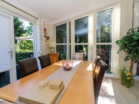 A dining area with a wooden table surrounded by chairs near large windows with a view of greenery at RoseGrace Lodge in Auchterarder