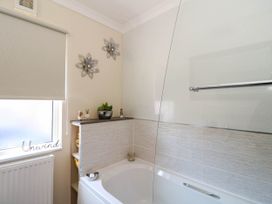 A bathroom with a bathtub, decorative flowers on the wall, a window with a roller blind, and small figurines on a shelf at RoseGrace Lodge in Auchterarder
