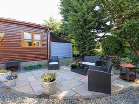 An outdoor patio with wicker chairs and a sofa around a glass coffee table next to a small fire pit and a wooden building at RoseGrace Lodge in Auchterarder