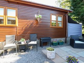An outdoor seating area with black chairs and a small table next to a brown wooden building at RoseGrace Lodge in Auchterarder