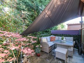 An outdoor seating area with a wicker corner sofa, table, and stools under a sunshade with plants around at RoseGrace Lodge in Auchterarder