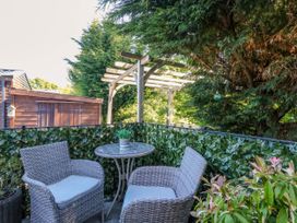An outdoor seating area with two chairs and a round table surrounded by greenery and a wooden shed at RoseGrace Lodge in Auchterarder