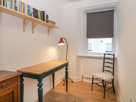 A small room with a wooden desk a black chair a floor lamp a window with a gray blind and a shelf with books at Saltwater Cottage in Babbacombe