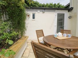An outdoor patio with a round wooden table and chairs next to a plant bed at Saltwater Cottage in Babbacombe