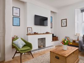 A living room with a green chair a wooden coffee table with flowers and a wall-mounted TV at Saltwater Cottage in Babbacombe