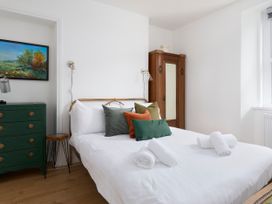 A bedroom with a bed with pillows and rolled towels a green dresser a wooden wardrobe and a painting at Saltwater Cottage in Babbacombe