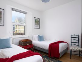 A bedroom with two single beds red blankets and blue pillows with a chair and framed pictures on the wall at Saltwater Cottage in Babbacombe
