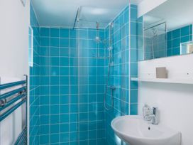 A bathroom with blue tiled shower area white sink mirror and chrome towel rail at Saltwater Cottage in Babbacombe