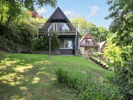 A sloped grassy garden with stairs leading to two wooden A-frame houses with balconies surrounded by trees at 60 Valley Lodge in Callington near Gunnislake