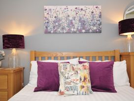 A bedroom with a wooden bed frame purple and floral pillows bedside table lamps and a floral painting on the wall at 60 Valley Lodge in Callington near Gunnislake