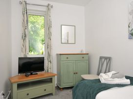A bedroom with a television on a stand a window with curtains a cupboard a chair and a bed with towels at 60 Valley Lodge in Callington near Gunnislake
