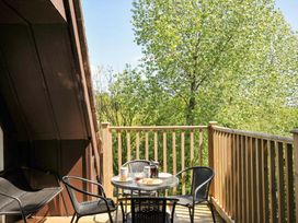 A balcony with a glass table and four black chairs surrounded by a wooden railing and trees at 60 Valley Lodge in Callington near Gunnislake