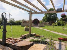 An outdoor scene with a hand water pump pouring water onto stones a wooden pergola two small wooden cabins on grass with pathways and plants at Lapwing Lodge in Cockerham near Lancaster