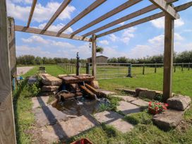 An outdoor wooden pergola with a stone water feature and a grassy field with a fence and a wooden shed in the background at Lapwing Lodge in Cockerham near Lancaster