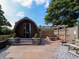 An outdoor area with a pod cabin entrance steps a hot tub wooden pergola picnic table and trees at Lapwing Lodge in Cockerham near Lancaster