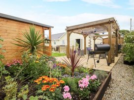 A garden with flowers and a grill under a pergola at Cae Berllan in Mynytho near Pwllheli