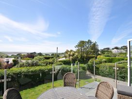 An outdoor area with a table and chairs overlooking greenery and houses at Farlands in Daymer Bay