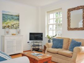 A living room with a beige sofa and blue cushions a wooden chest coffee table a white cabinet with artwork above and a television on a stand by the window at Lowenna Manor 3 in Rock