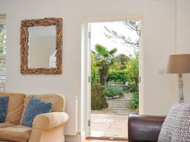 A living room with a beige sofa with blue cushions a brown armchair with a patterned cushion a lamp and a wooden framed mirror with a door opening to a garden at Lowenna Manor 3 in Rock