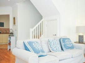 A living area with a white sofa and blue patterned cushions a small side table with a lamp a staircase and a kitchen view at Lowenna Manor 3 in Rock