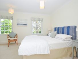 A bedroom with a bed with blue patterned headboard two windows a wicker chair and bedside tables at Lowenna Manor 3 in Rock