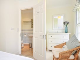 A bedroom with a wicker chair, white chest of drawers, mirror, and an open door to a bathroom at Lowenna Manor 3 in Rock