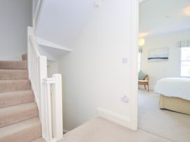 A carpeted staircase leading to a hallway with an open door to a bedroom with a bed a wicker chair and wall art at Lowenna Manor 3 in Rock
